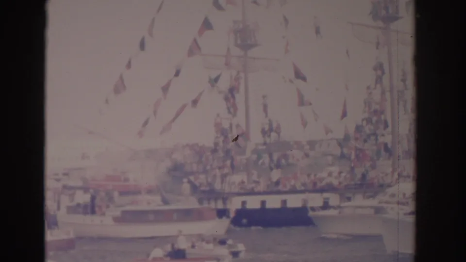 1962 Florida harbor scene with a flag-covered ship, spectators on deck, and small boats gathered around the waterway.