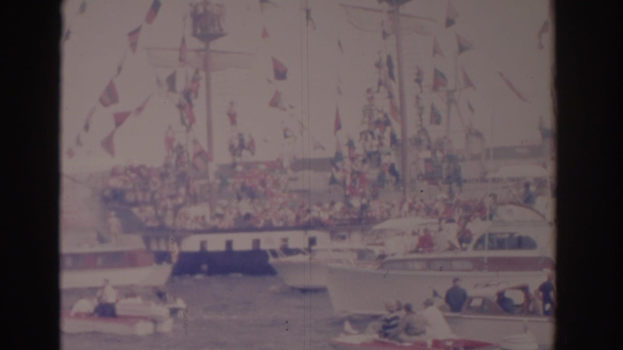 A decorated ship in a Florida harbor is surrounded by small pleasure boats and distant spectators in faded 8mm color.