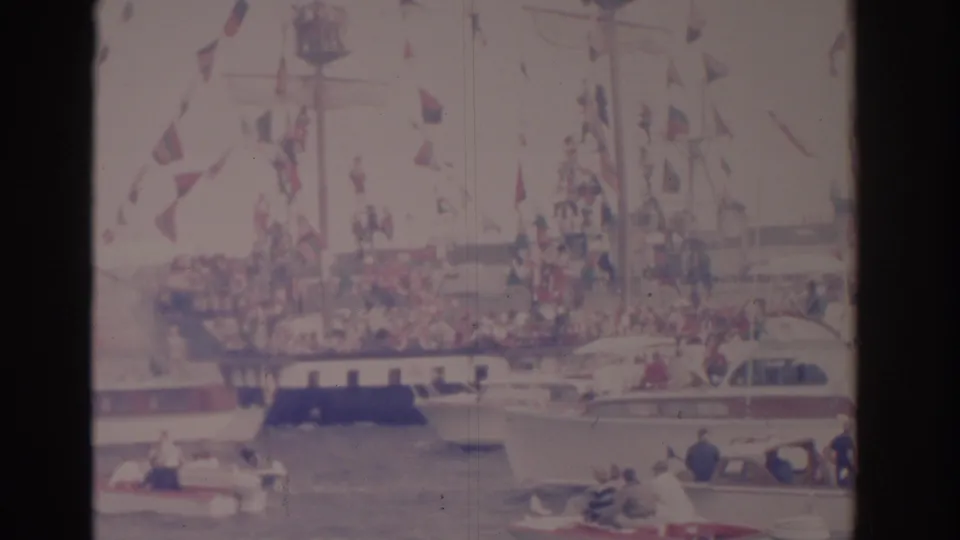 A decorated ship in a Florida harbor is surrounded by small pleasure boats and distant spectators in faded 8mm color.