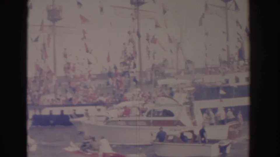 A small motorboat crosses the foreground while a crowded flag-decorated ship remains behind it in the 1962 Florida harbor footage.