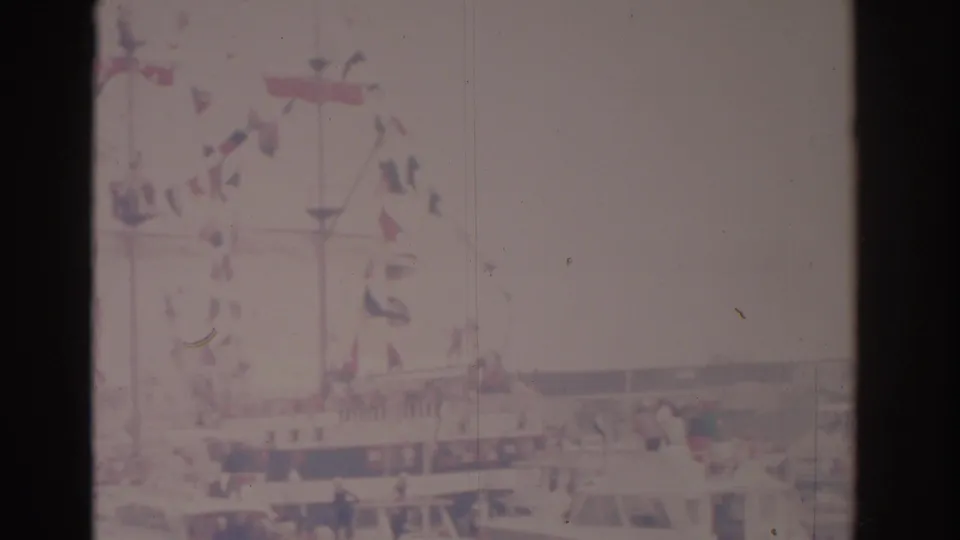 Faded 8mm frame from the supplied 1962 Florida clip showing a bright street area with flags or bunting, cars, and distant roadside activity.