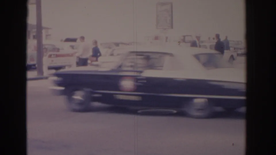 1962 Florida street view with a dark car blurred in motion, parked classic cars, and pedestrians near the curb.