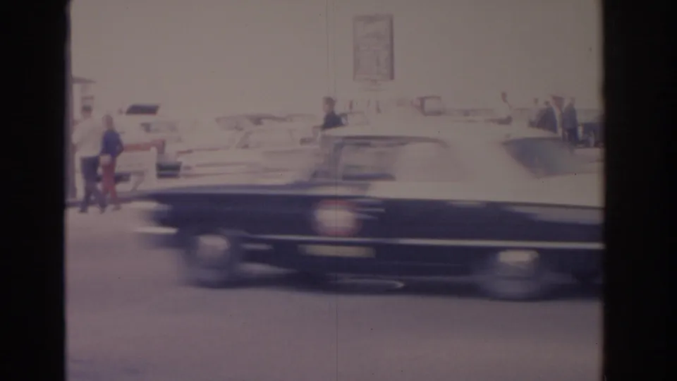 A large dark car crosses the 1962 Florida frame with pedestrians and light-colored parked cars behind it.