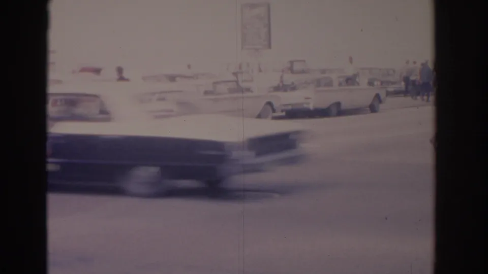 Motion-blurred foreground car crosses a Florida street scene with classic parked cars and pedestrians beyond.