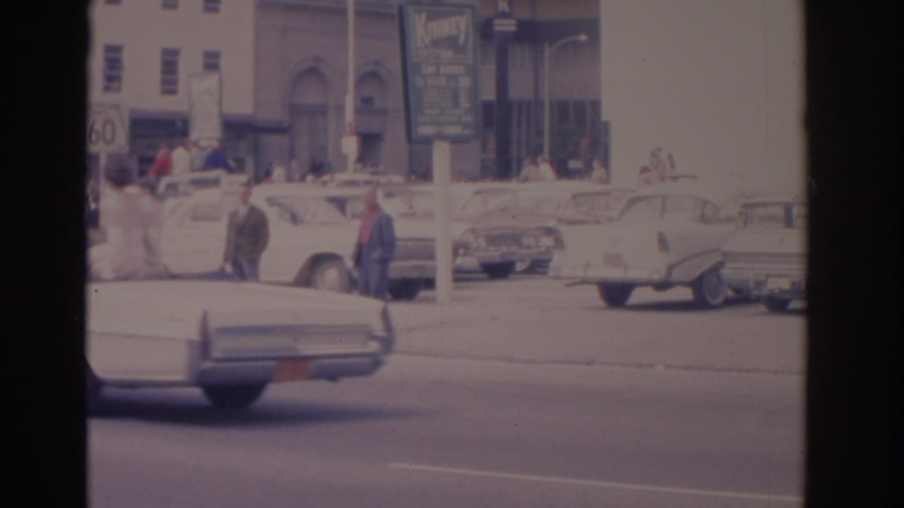 Florida street with pedestrians, parked cars, a Kinney System sign, and a passing white car.
