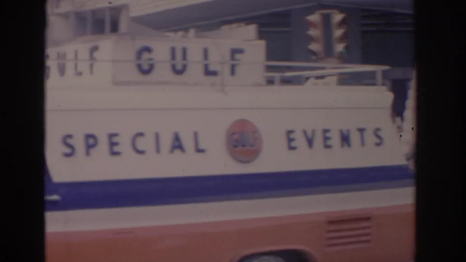 The Gulf Special Events vehicle continues past the camera in 1962 Florida footage, with a traffic signal and building facade behind it.