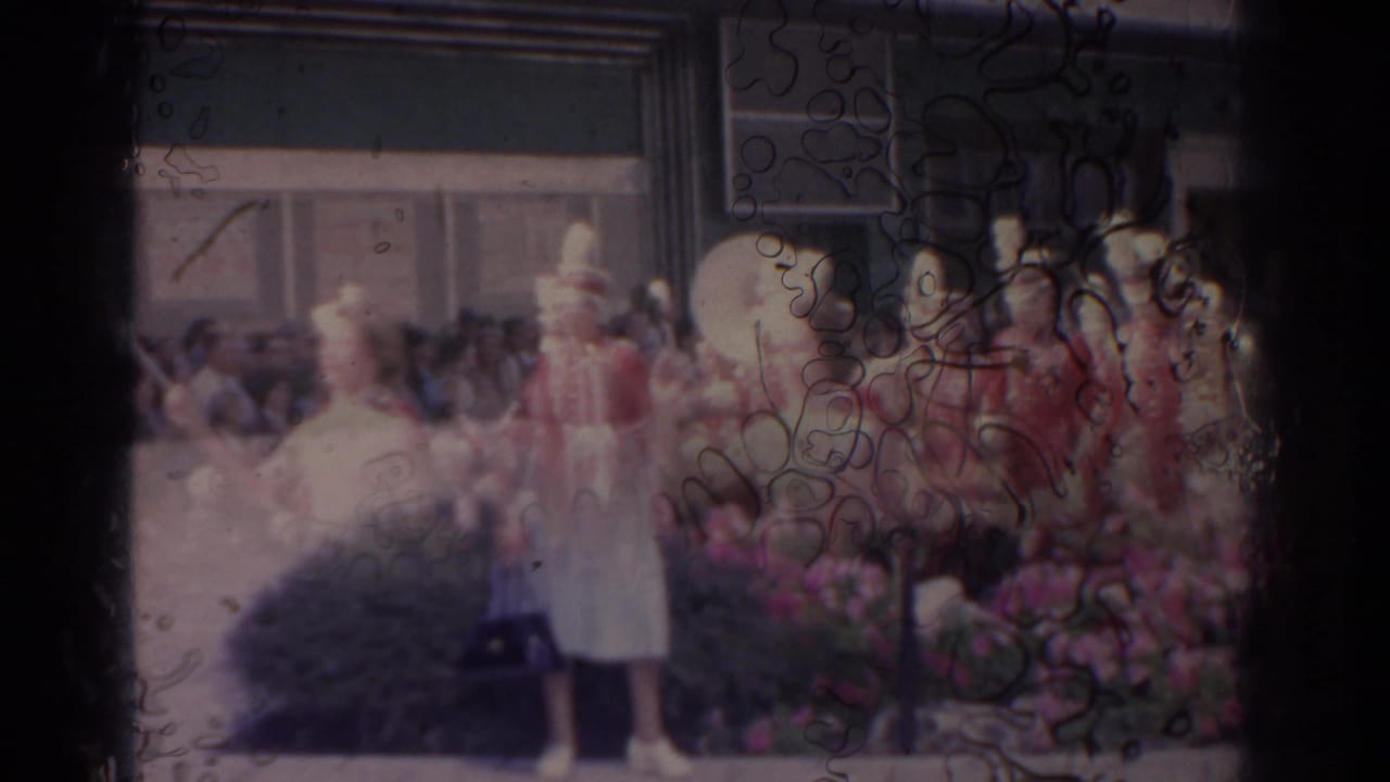 Parade performers in red uniforms and a white-clad majorette before spectators.
