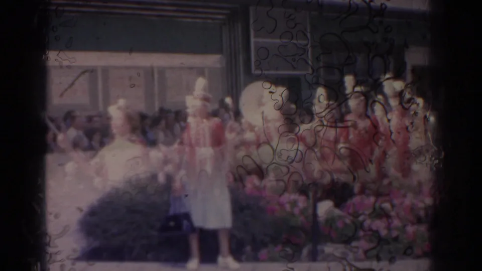 Soft 8mm frame of a Florida parade scene with red-uniformed performers, a white-clad majorette, and spectators in the background.