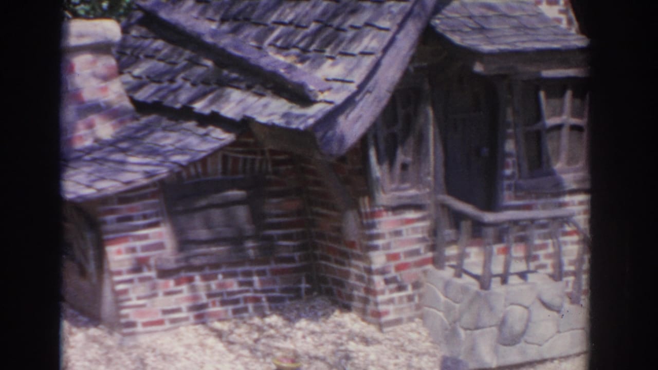 1962 Florida 8mm frame with the miniature cottage filling the view, showing brickwork, a chimney, a dark doorway, and small windows.