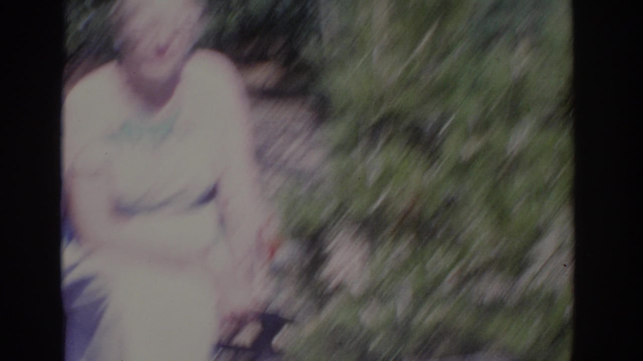 Blurred woman in a pale dress seated outdoors among greenery.