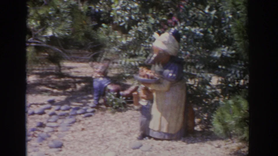 1962 Florida 8mm frame with a carved bear-like statue wearing an apron near dense greenery and a smaller wooden figure.