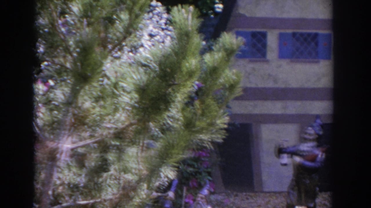 Miniature house partly obscured by greenery with a gnome figure holding a bottle.