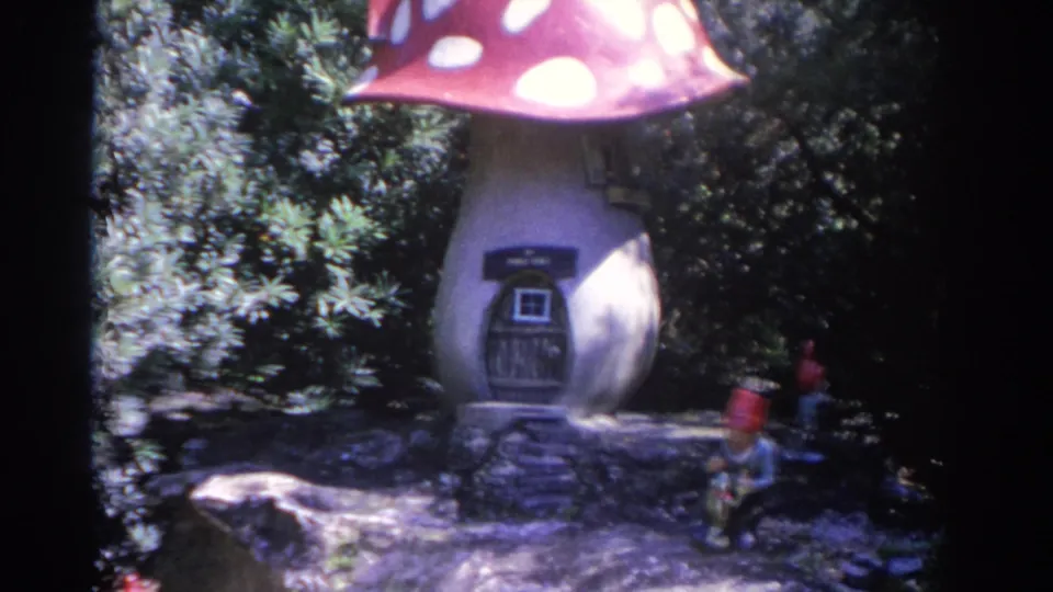The mushroom-shaped garden house is shown more fully, with a small doorway, stone edging, and a gnome figure to the right.