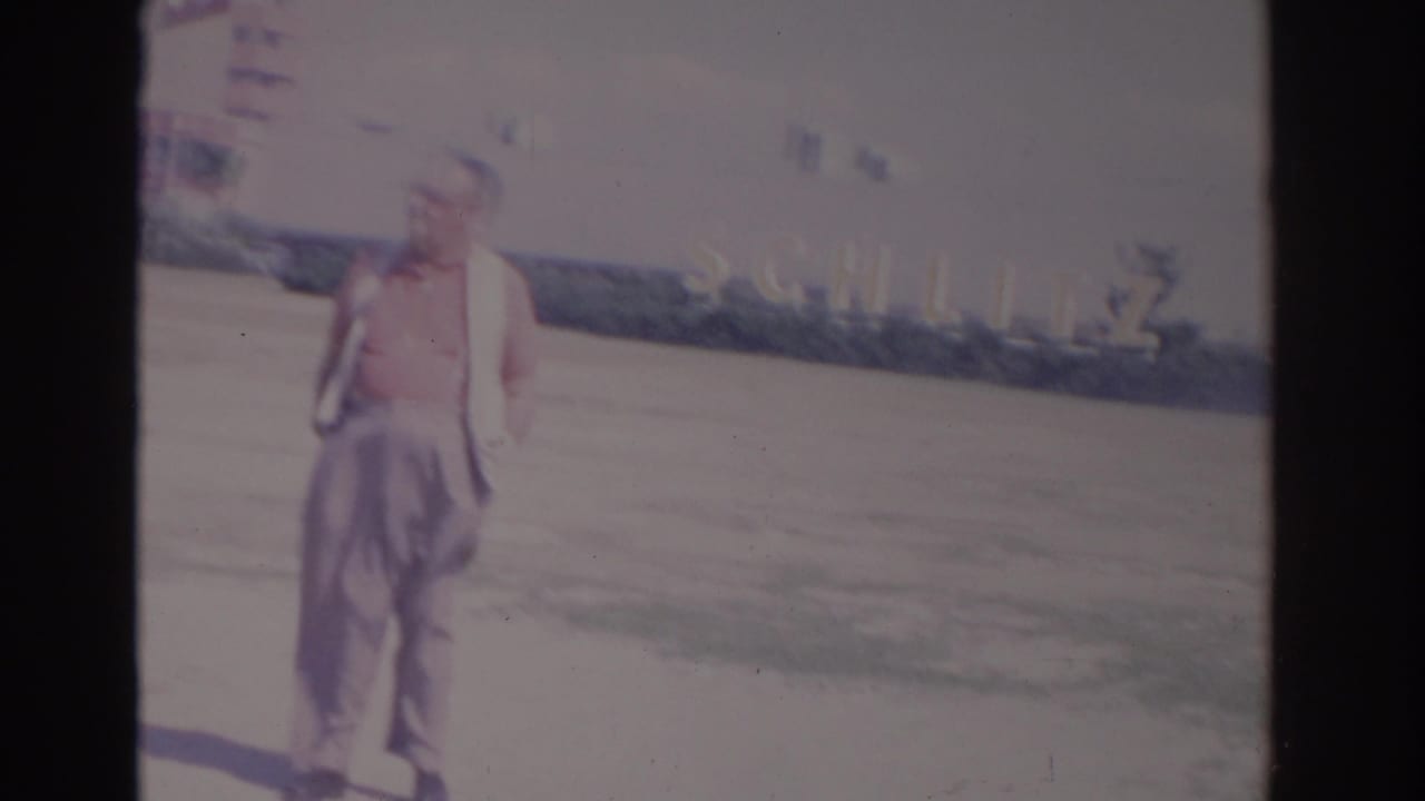 Man in a red shirt standing or walking near a broad roadside area.
