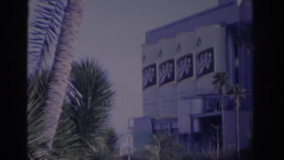 1962 Florida 8mm frame showing a branded commercial building exterior behind palm trees and dark film-edge borders.