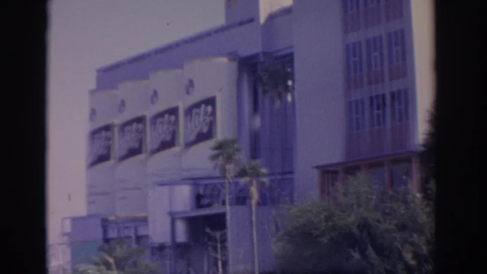 1962 Florida 8mm view of the branded building facade, palm trees, shrubbery, and adjacent vertical wall sections.