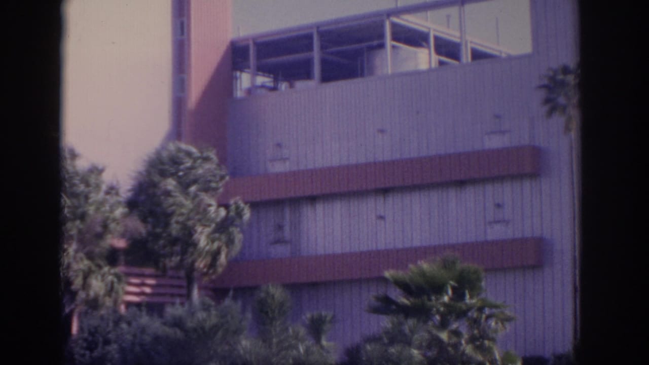 Mid-century building with palm trees and red horizontal bands.