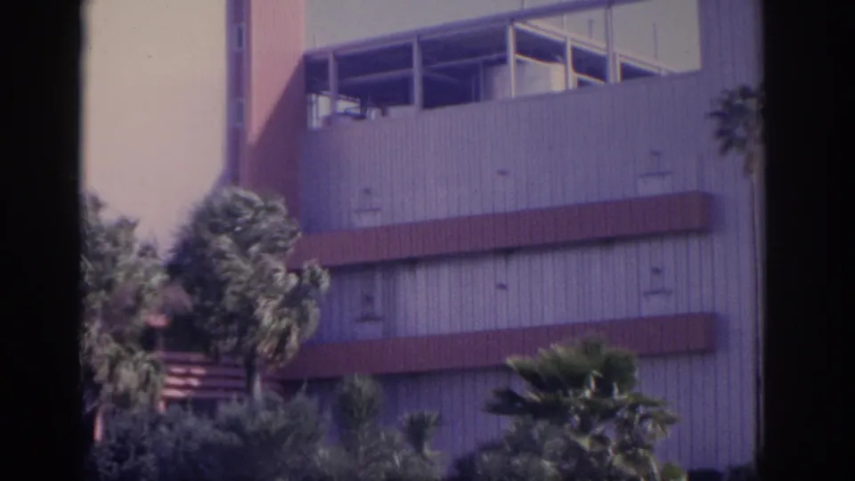 1962 Florida 8mm frame showing a mid-century exterior with palm landscaping, red horizontal bands, and visible film borders.