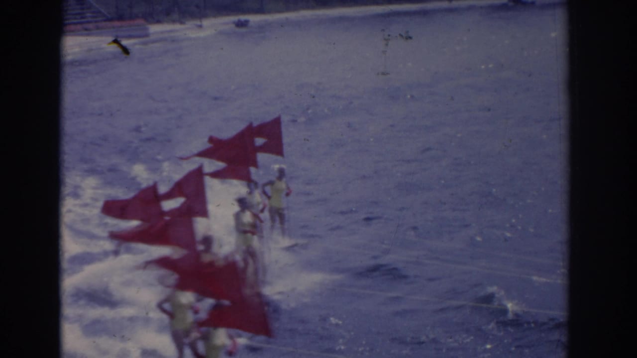 Surfers ride choppy waves near several red triangular flags in the water.