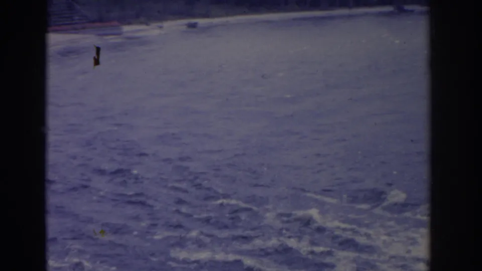 The frame holds mostly choppy ocean water and foam, with a faint shoreline near the top in faded home-movie color.