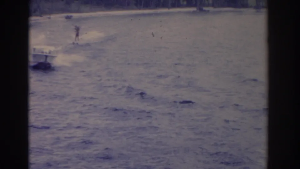 1962 Florida 8mm frame showing a distant water skier behind a white speedboat on a lake with a foamy wake.