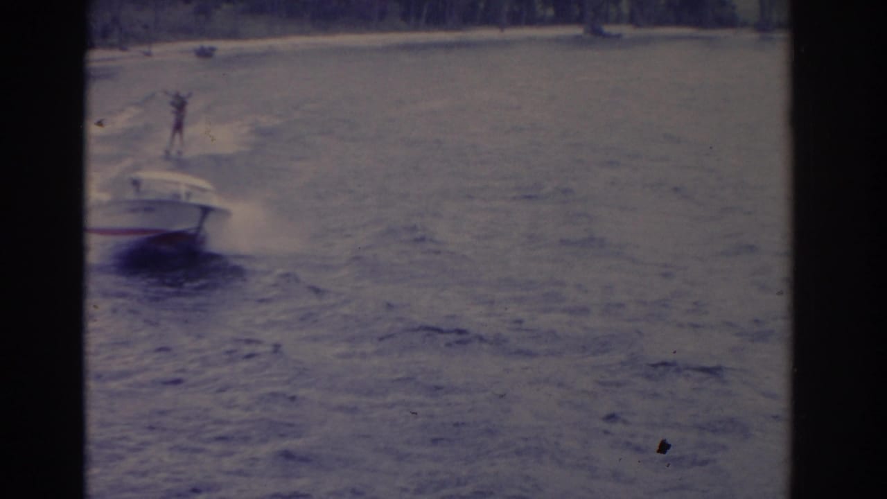 Speedboat moves across choppy water while a distant skier rides in its wake.