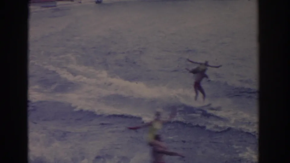 1962 Florida home-movie frame with a distant skier on the water and a soft, passing foreground figure.