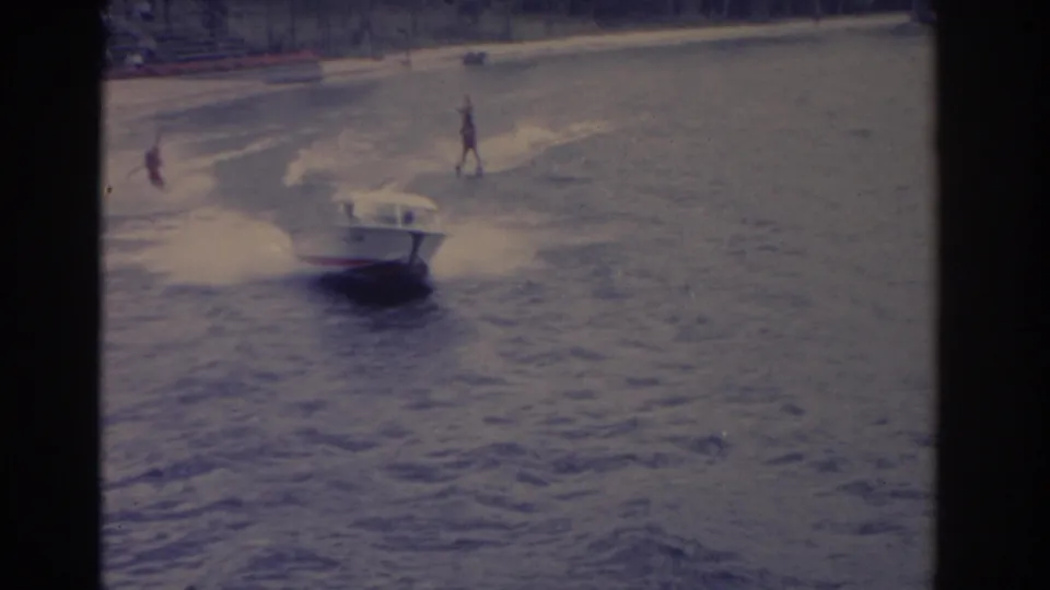 1962 Florida 8mm frame showing a small motorboat on open water with distant skiers behind it.