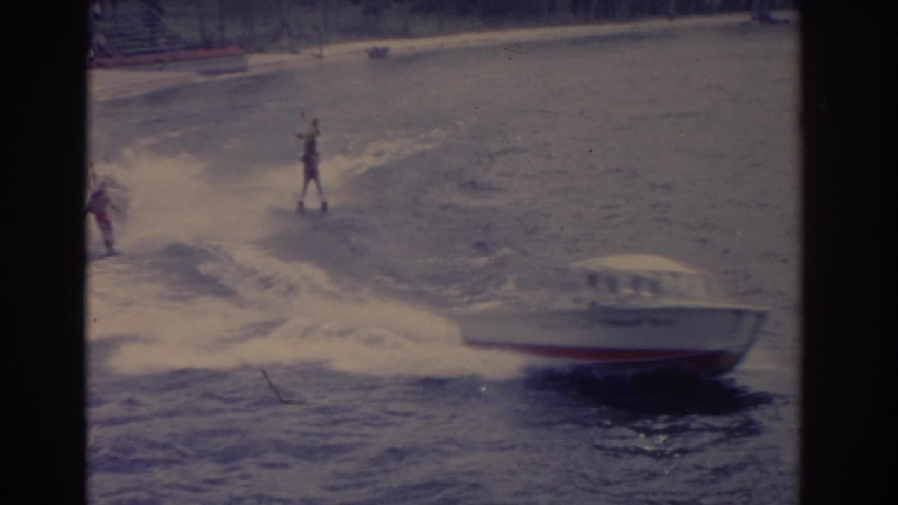 Motorboat passes at right while a water skier rides behind with arms raised.