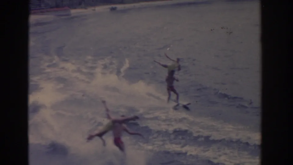 1962 Florida home-movie frame with one skier still upright and another skier falling into the spray-filled wake.