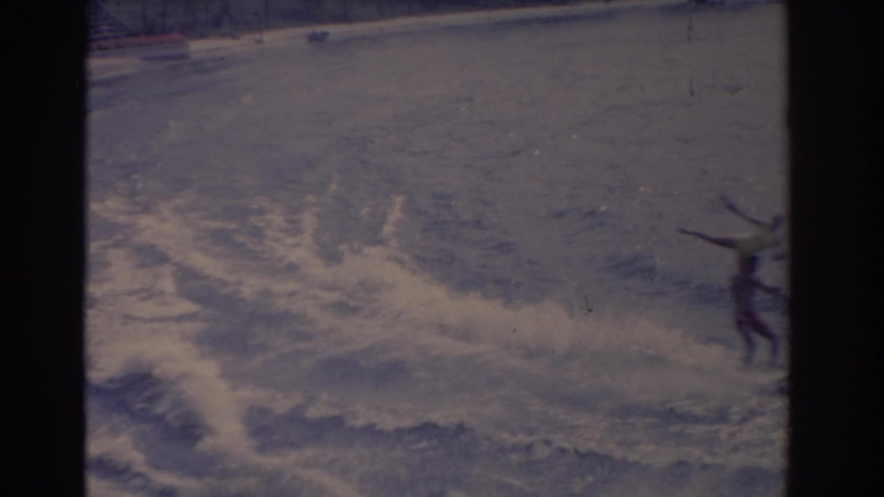 A waterskier cuts across choppy water with white spray near a distant shoreline.