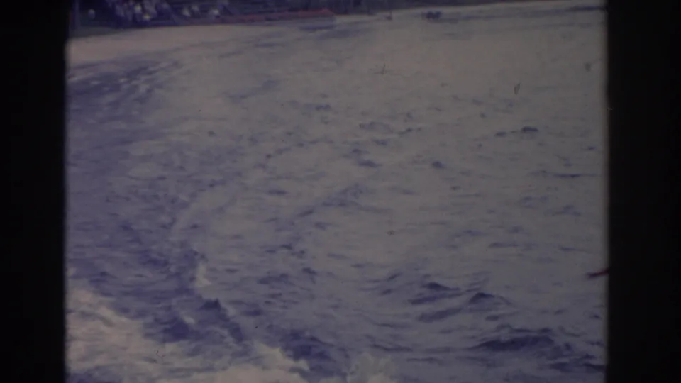 A soft 8mm frame shows textured lake water and wake after the water ski formation moves out of the shot.