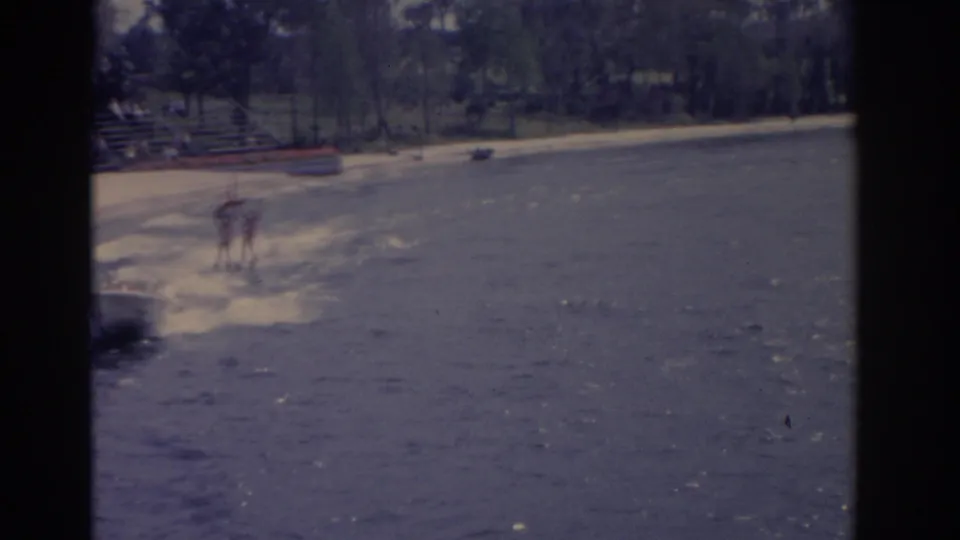The water skiers appear farther away near the tree-lined shore in this 1962 Florida 8mm home-movie frame.