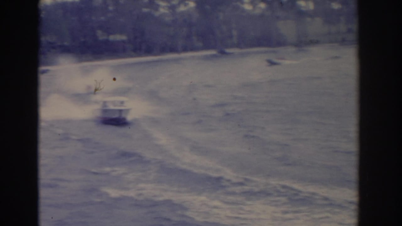 Small motorboat speeds across choppy water, leaving a broad wake within dark 8mm frame borders.