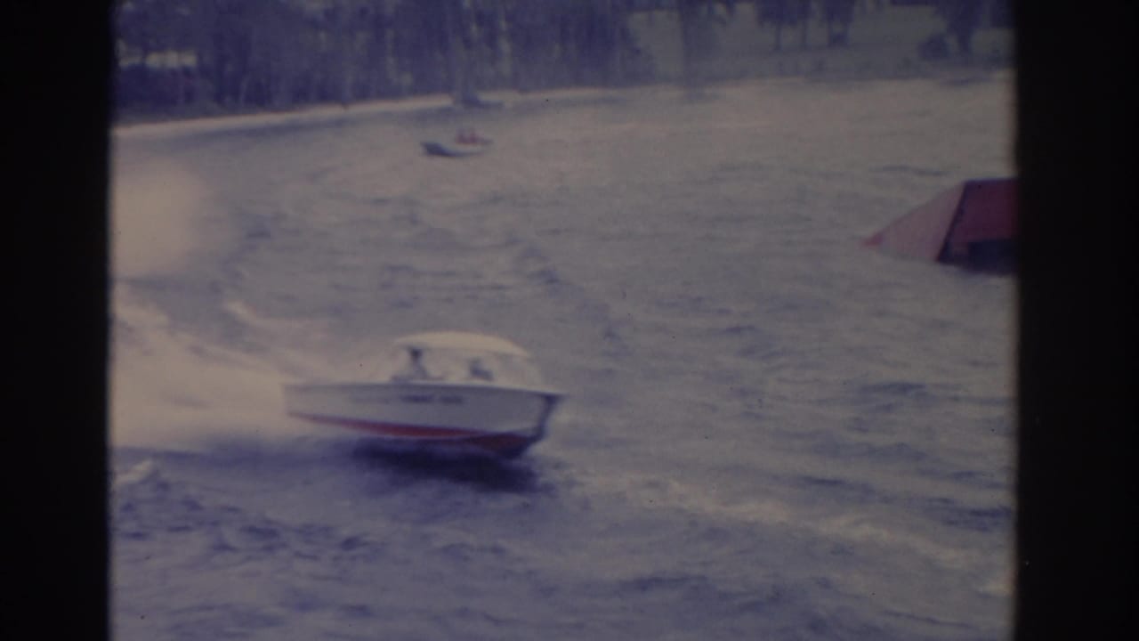 1962 Florida 8mm frame with a motorboat cutting through rough water while distant small craft sit near the far shore.