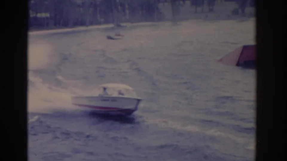 1962 Florida 8mm frame with a motorboat cutting through rough water while distant small craft sit near the far shore.