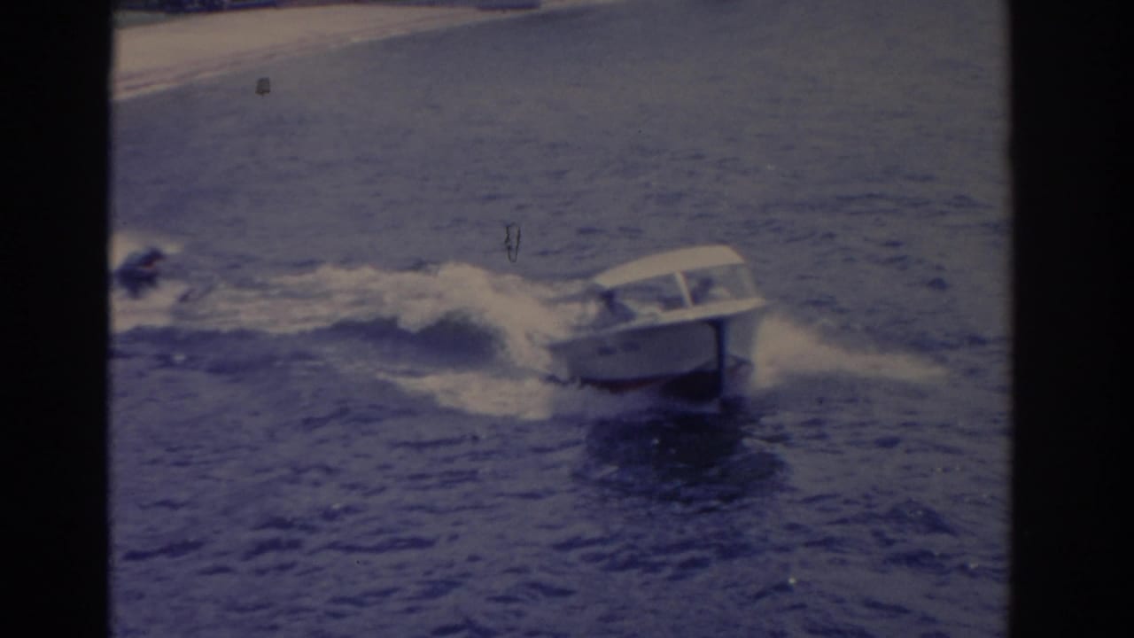 White motorboat speeds across choppy water near a distant shoreline.