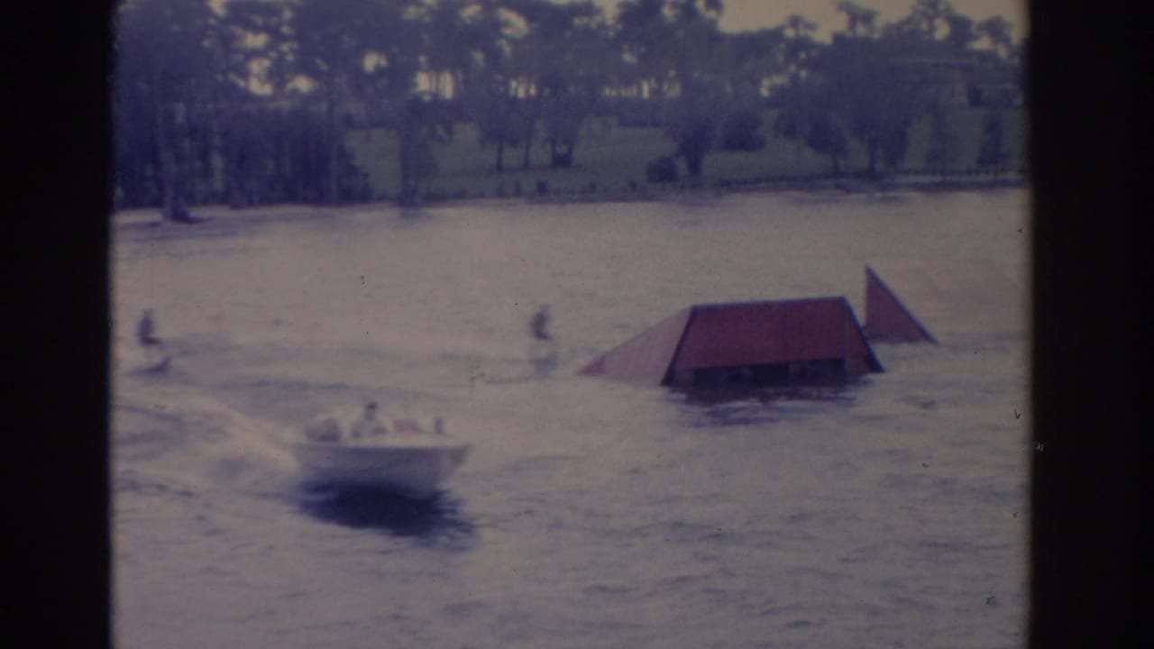 1962 Florida frame showing a boat near a floating ramp, with distant people and trees along the waterline.