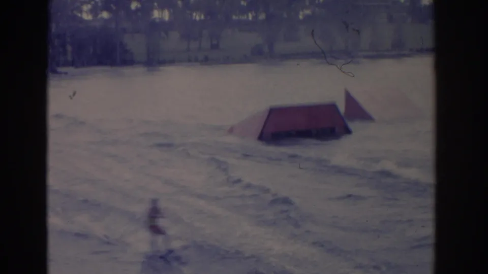 1962 Florida water-ski scene with a distant skier passing near a red ramp on a lake, with trees along the far shore.