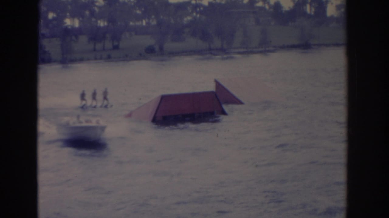 1962 Florida 8mm frame showing a motorboat pulling several distant skiers past a red ramp on choppy water.