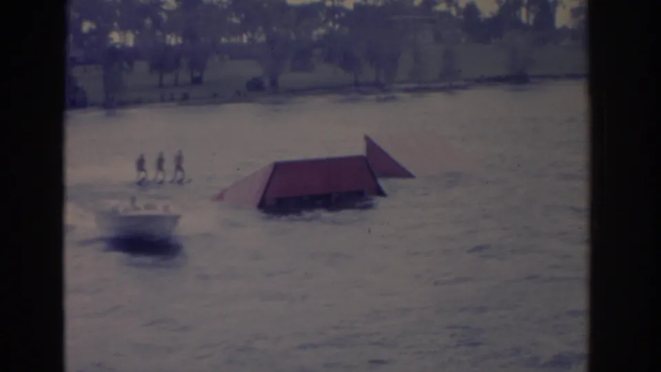 1962 Florida 8mm frame showing a motorboat pulling several distant skiers past a red ramp on choppy water.