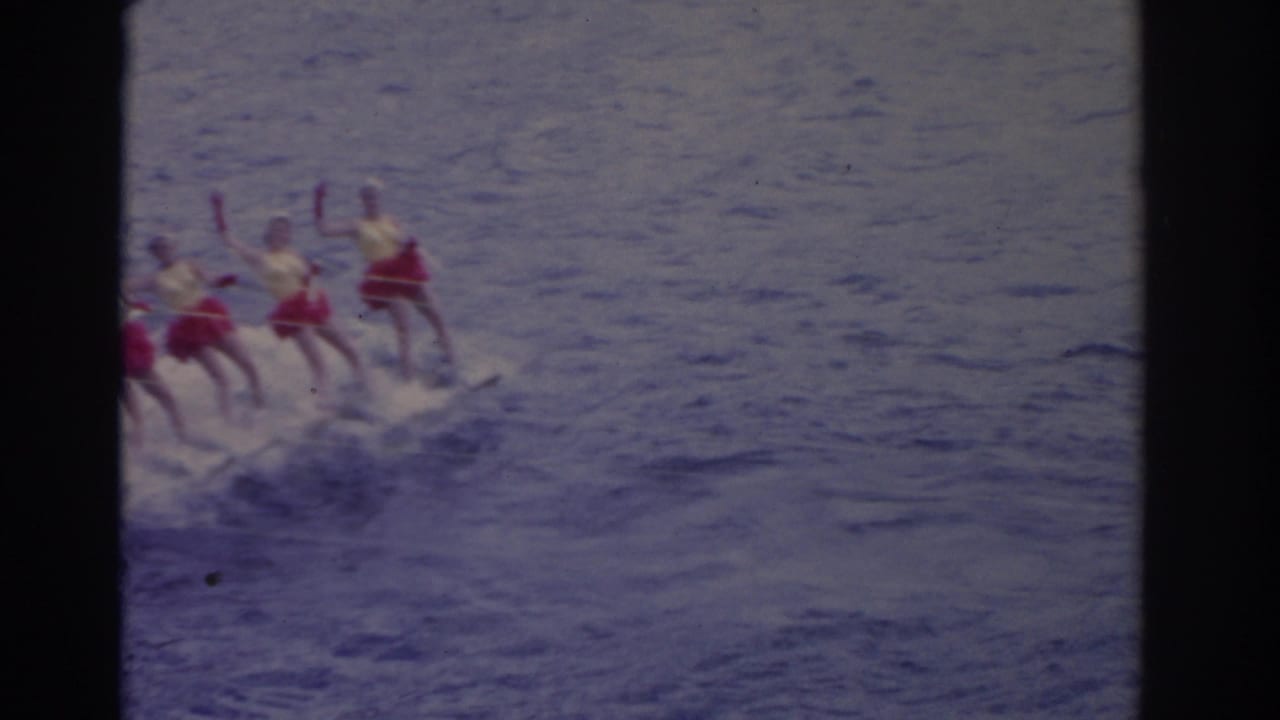 1962 Florida 8mm frame showing several women in bright swimsuits skiing together across open water behind a tow boat offscreen.