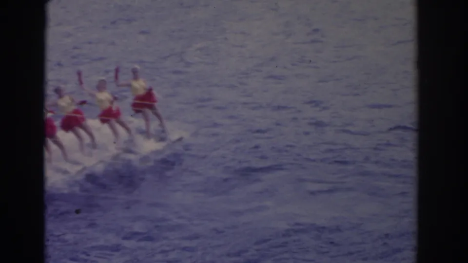 1962 Florida 8mm frame showing several women in bright swimsuits skiing together across open water behind a tow boat offscreen.