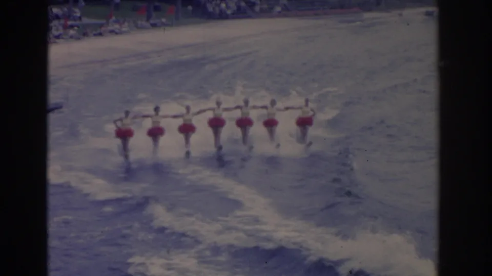 In 1962 Florida home-movie footage, a line of female water skiers in red skirts and white tops glides across the water.