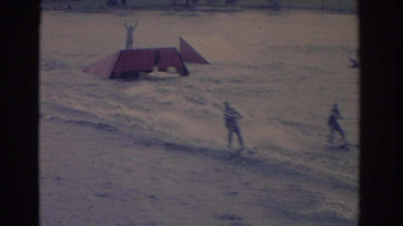 Two skiers move past a floating red-roofed platform as the spectator-shot 1962 Florida water show continues.