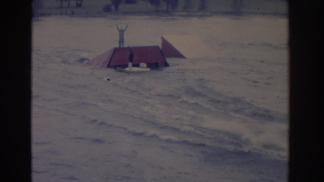 Red floating ramp on choppy water with a person standing with arms raised.