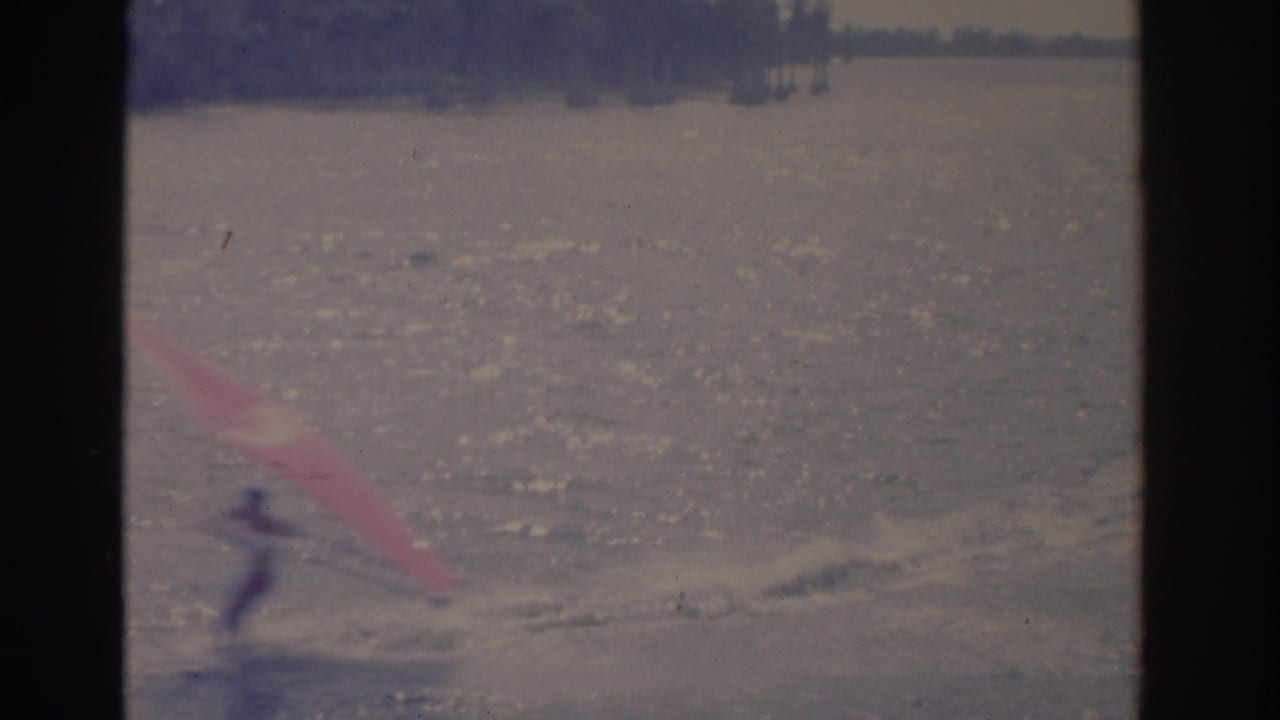 A distant figure appears to speed across a Florida lake with a red sail, leaving disturbed water behind in the 8mm frame.