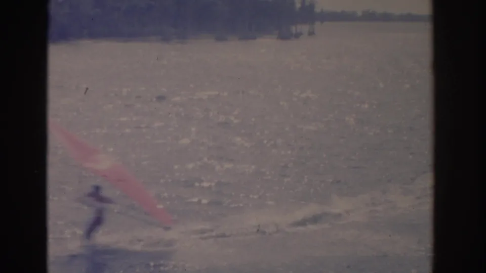 A distant figure appears to speed across a Florida lake with a red sail, leaving disturbed water behind in the 8mm frame.