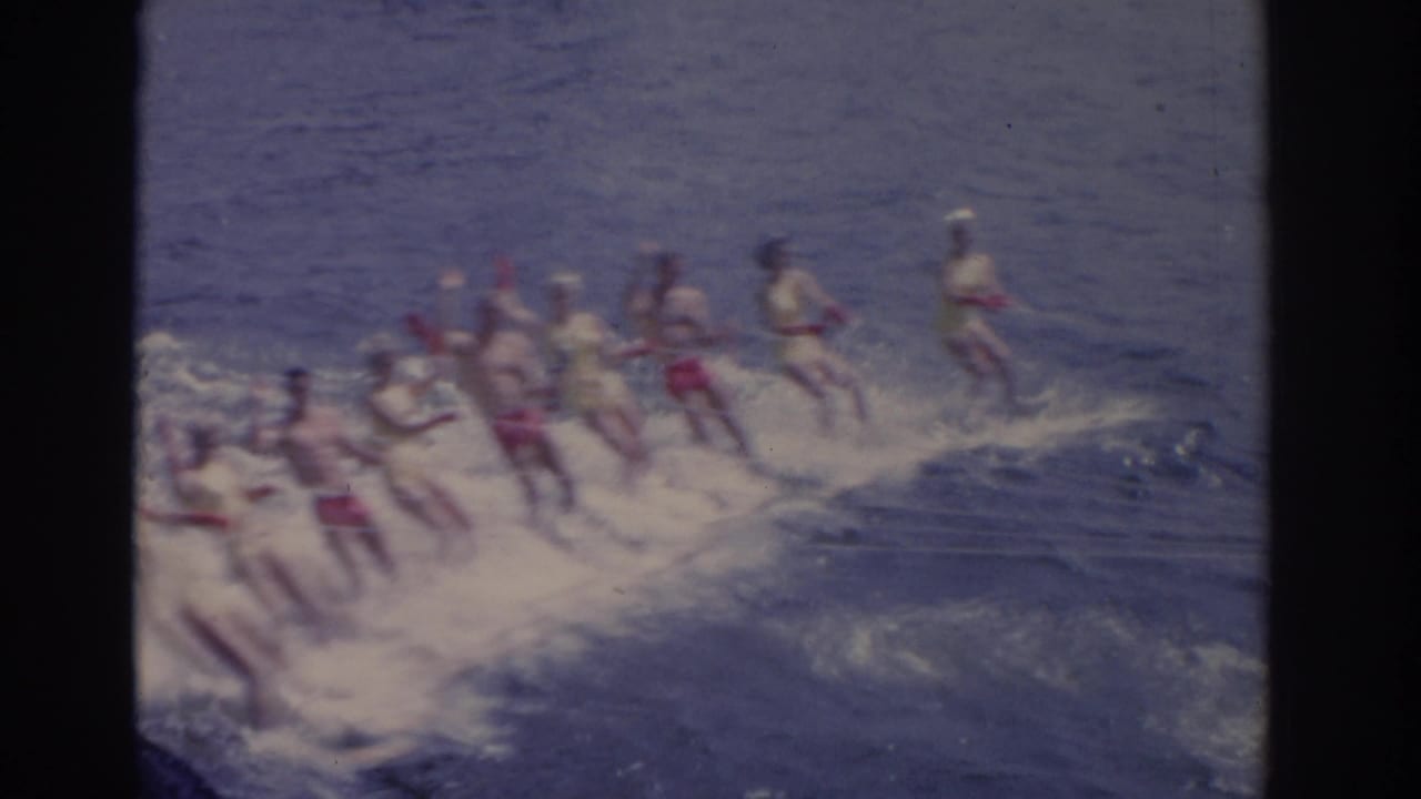 A group of people water ski together across a Florida lake, their bright swimwear visible through soft 8mm color and grain.