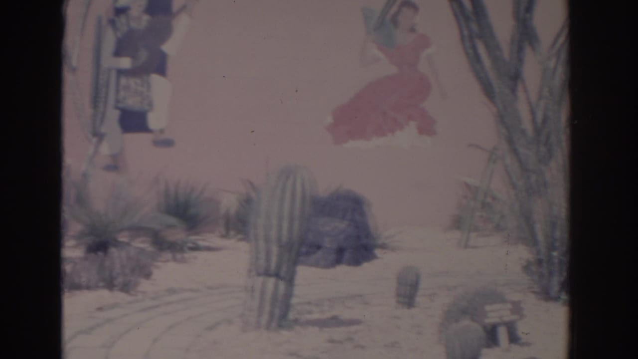 1962 Florida 8mm view of a cactus garden beside a pink wall with painted figures, including a woman in a red dress.